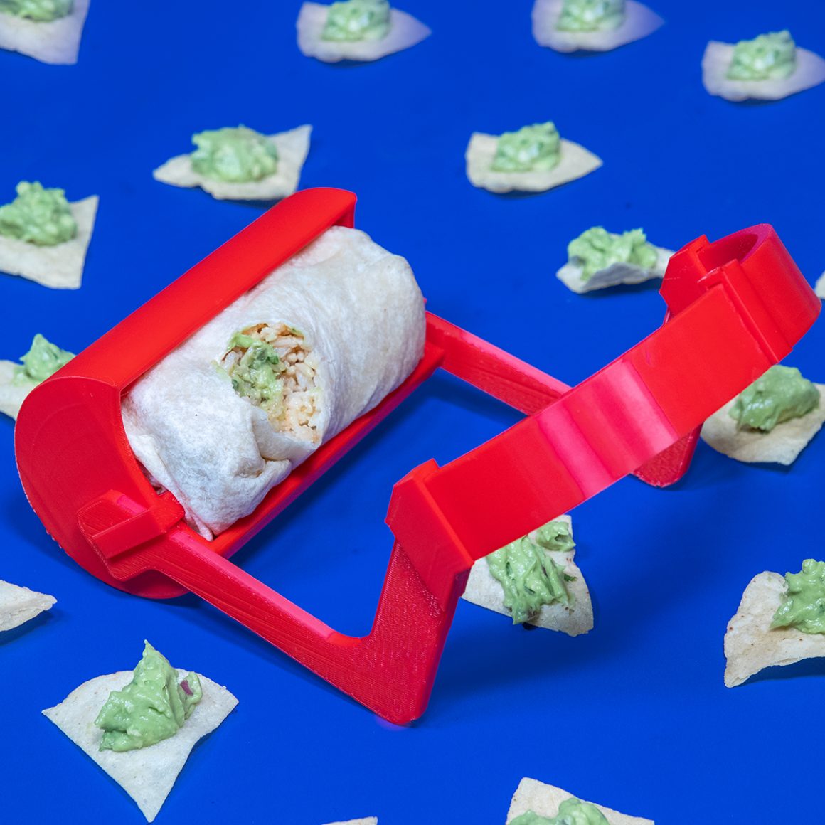 A burrito resting in a red support frame surrounded by pieces of lettuce.