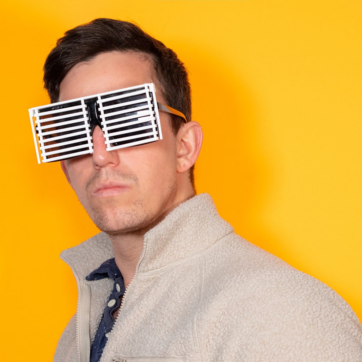Matty wearing sunglasses covered by white slatted blinds.