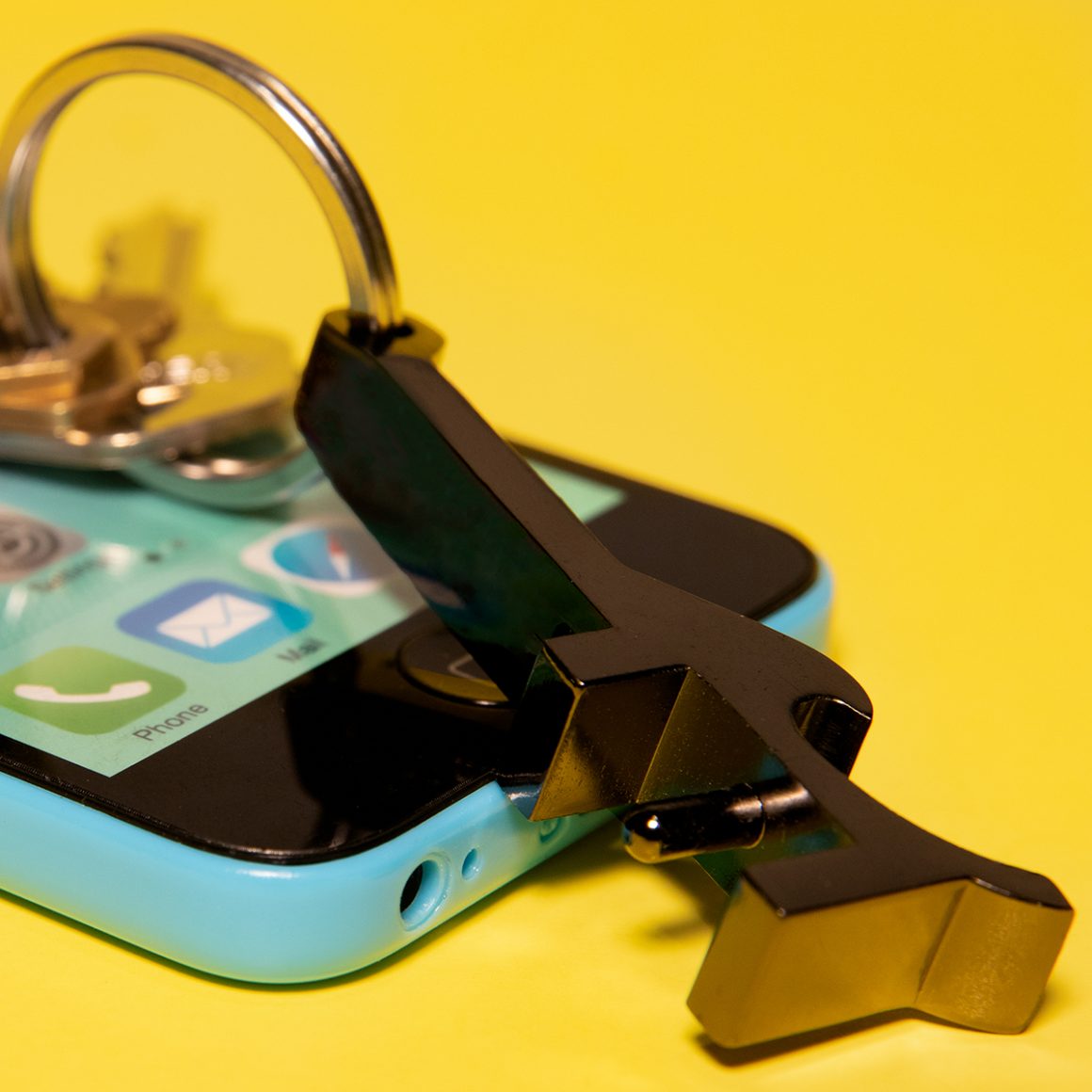 A black keychain tool fitted into the headphone port of a patterned phone case.