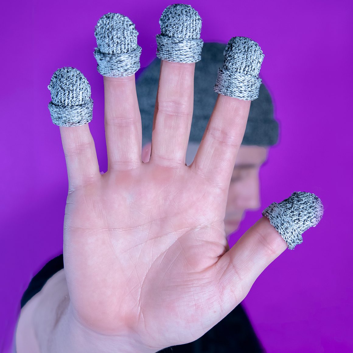 A raised hand wearing five tiny gray knitted hats on its fingertips.