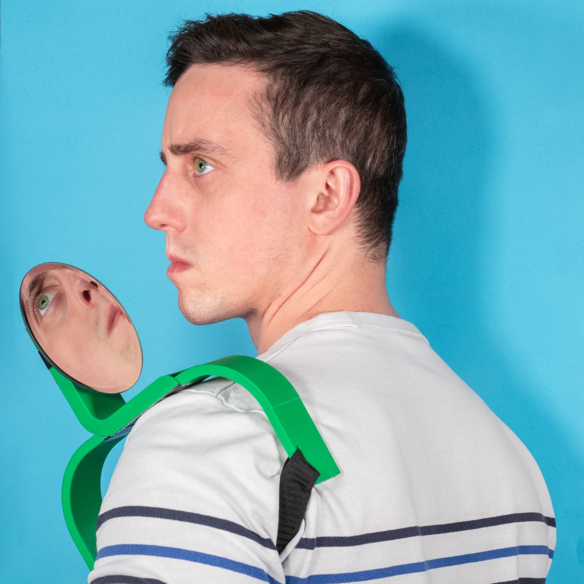 Matty looking back beside a circular mirror on a green shoulder mount.