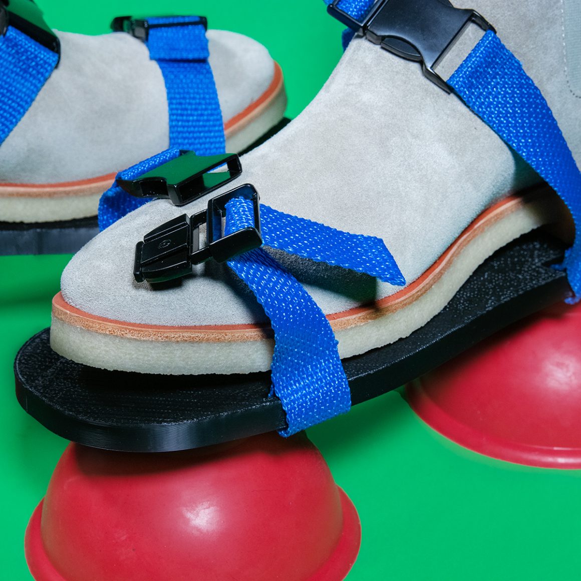 A light-colored shoe strapped onto a black platform above red suction cups.