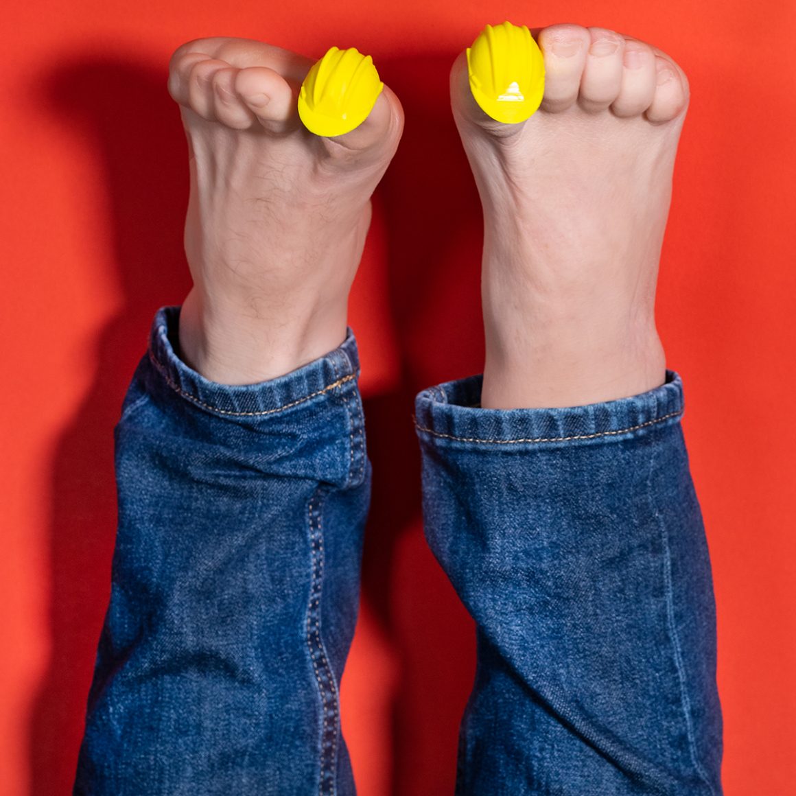 Feet wearing small yellow hard-hat-shaped caps on the big toes.