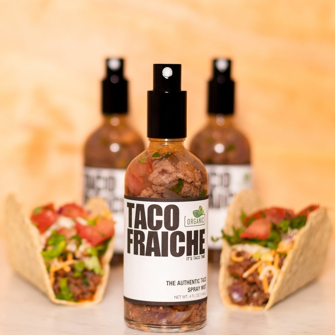 Small spray bottles labeled Taco Fraiche arranged beside tacos.