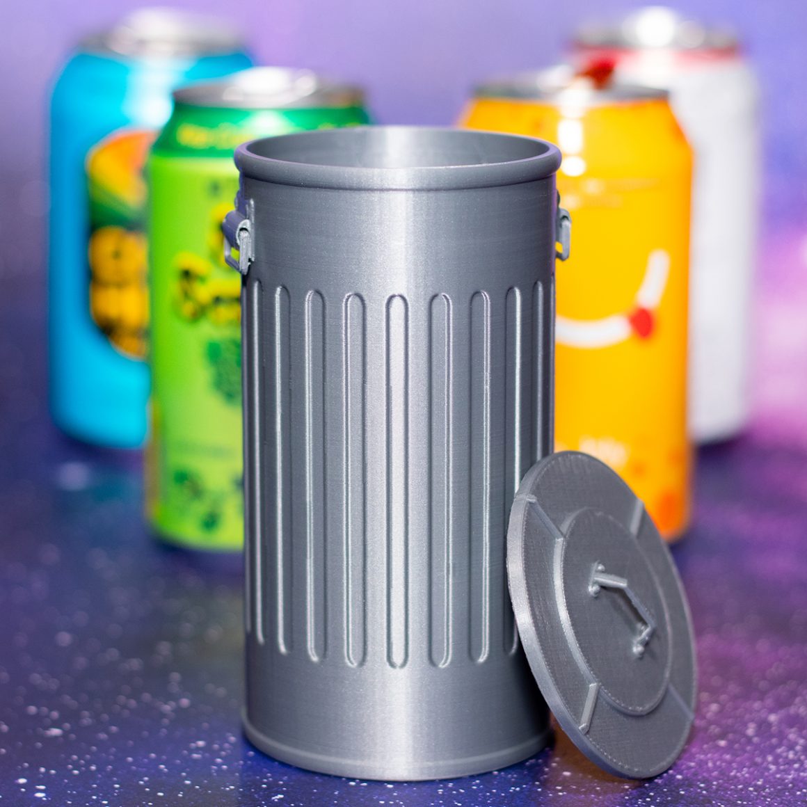 A tiny gray trash can with its lid leaning against the side.
