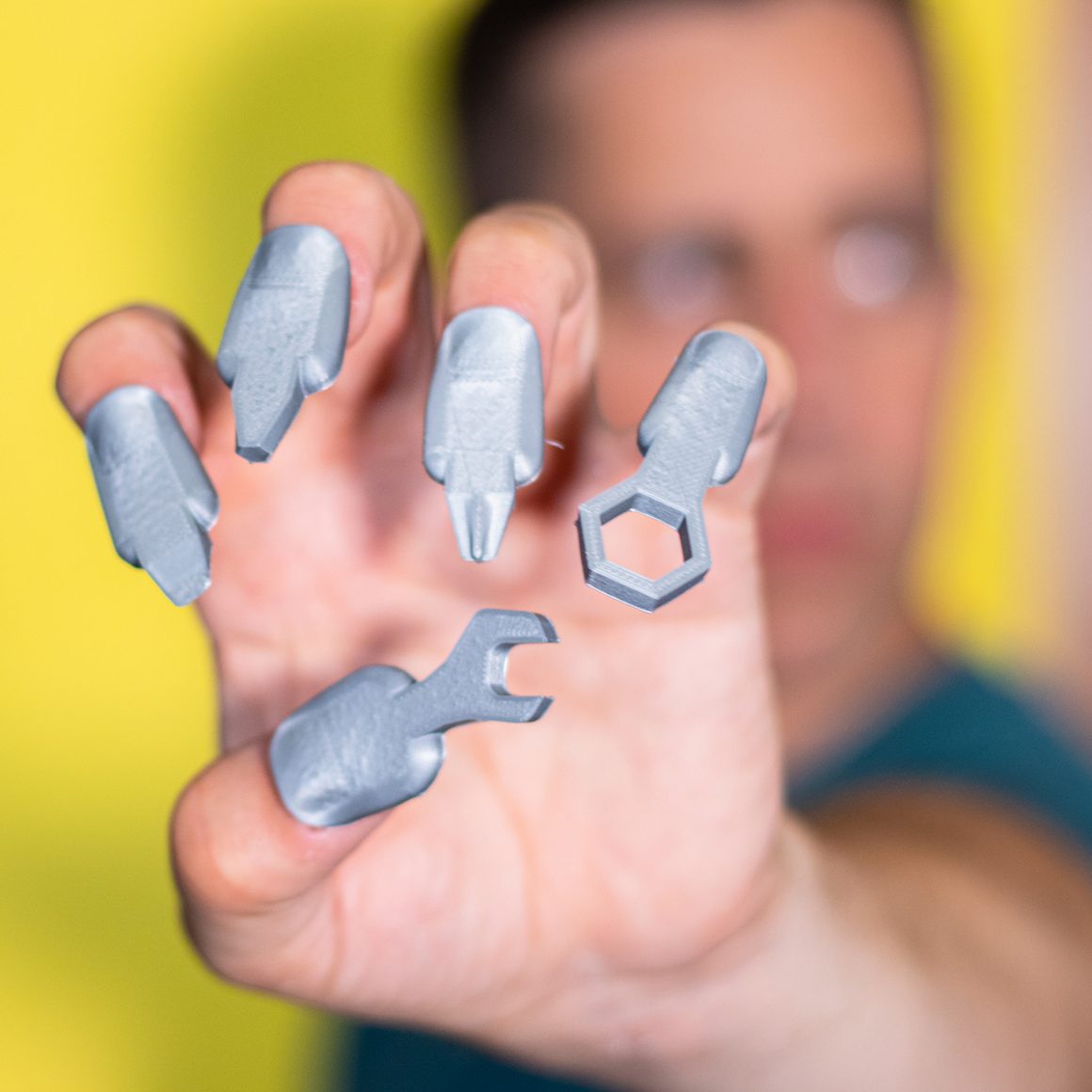Matty displaying metallic nail attachments with wrench and screwdriver-shaped tips.