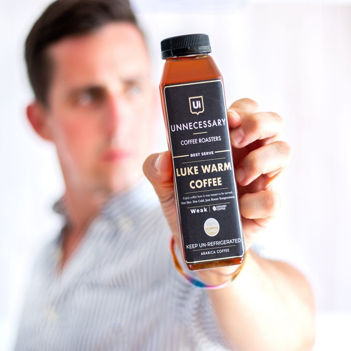 Matty holding a bottle labeled Luke Warm Coffee toward the camera.