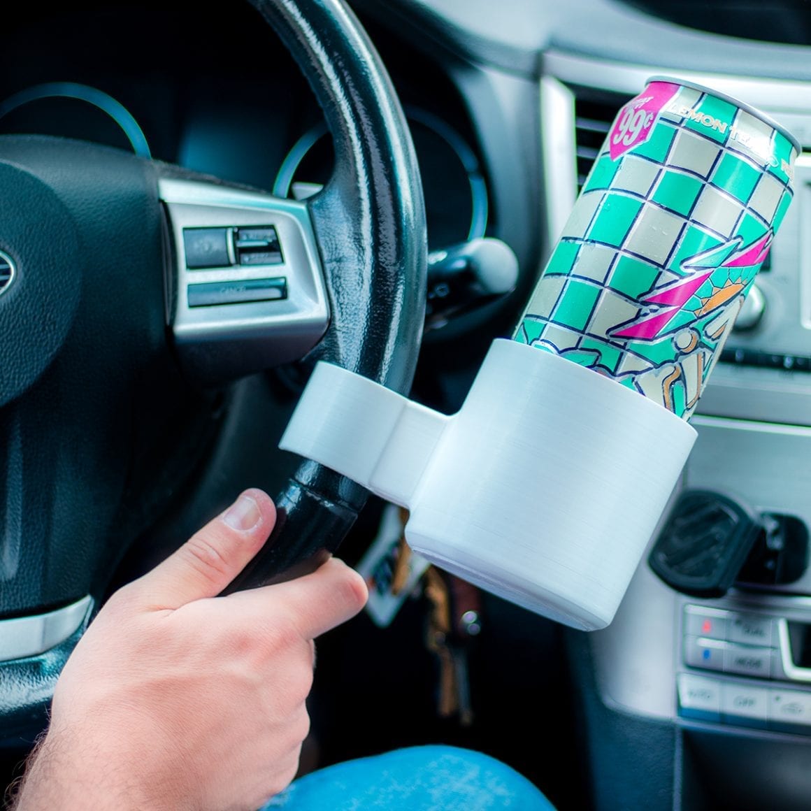 A white cup holder clipped to a steering wheel and holding a patterned tumbler.
