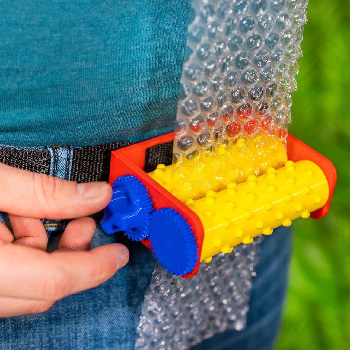 A colorful belt buckle feeding a strip of bubble wrap through yellow rollers.