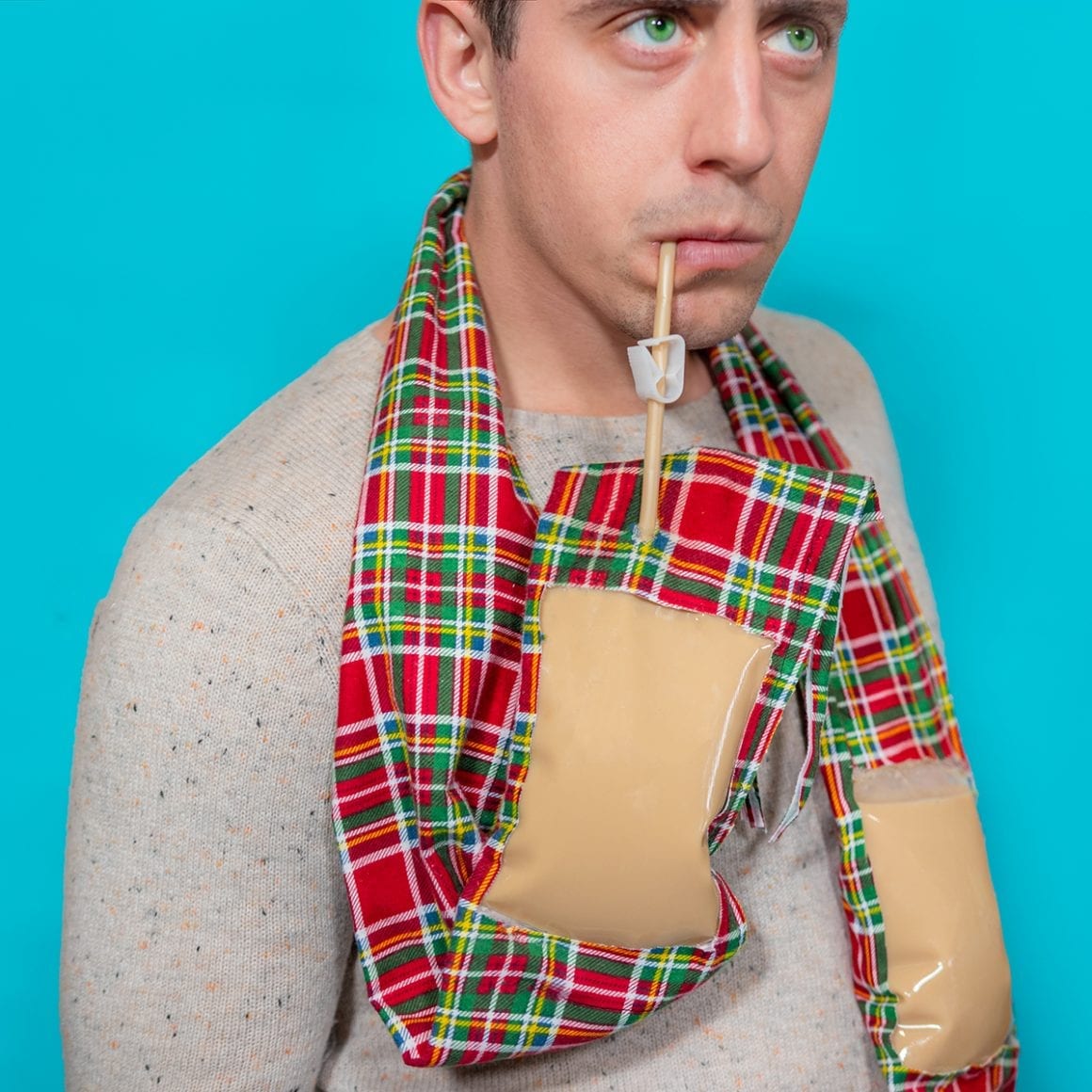 Matty sipping through a straw from a drink pouch built into a red plaid scarf.
