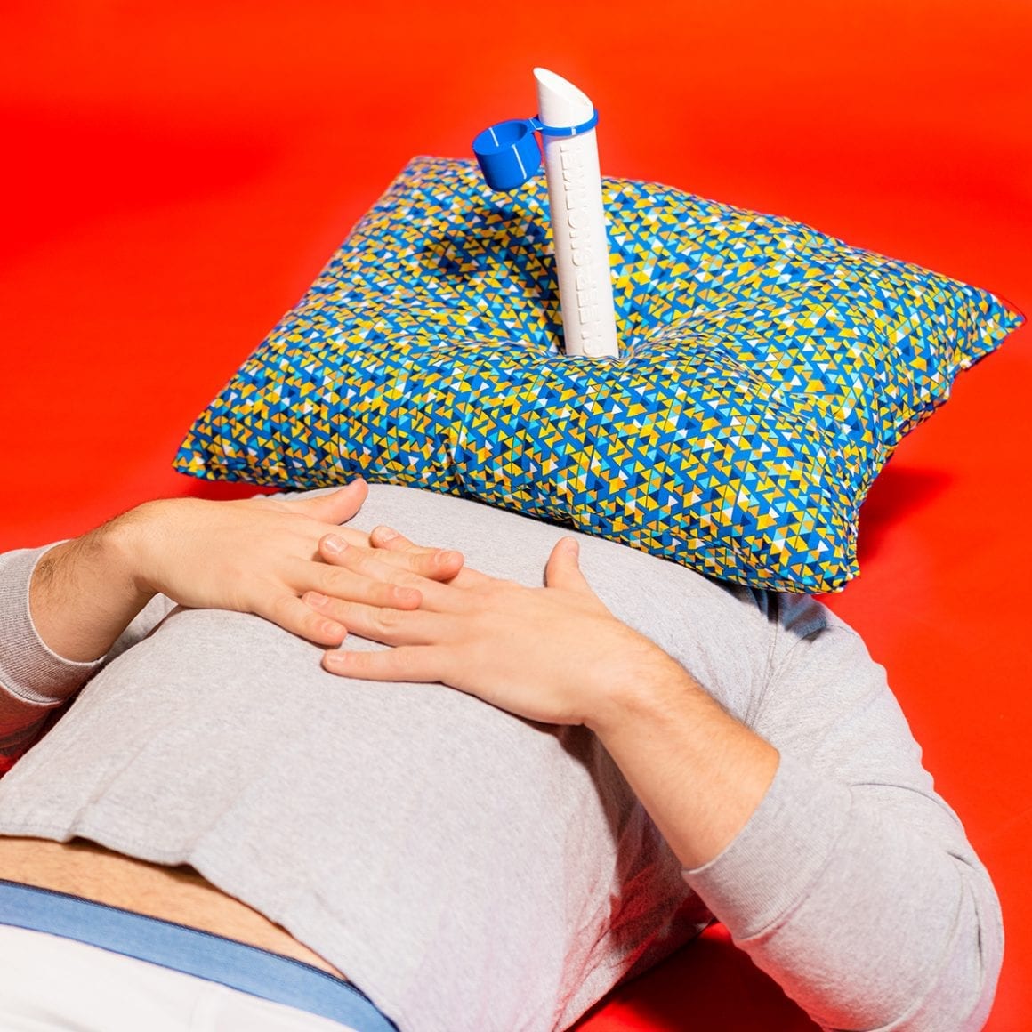 Matty lying down with a patterned pillow over his face and a tube projecting from its center.
