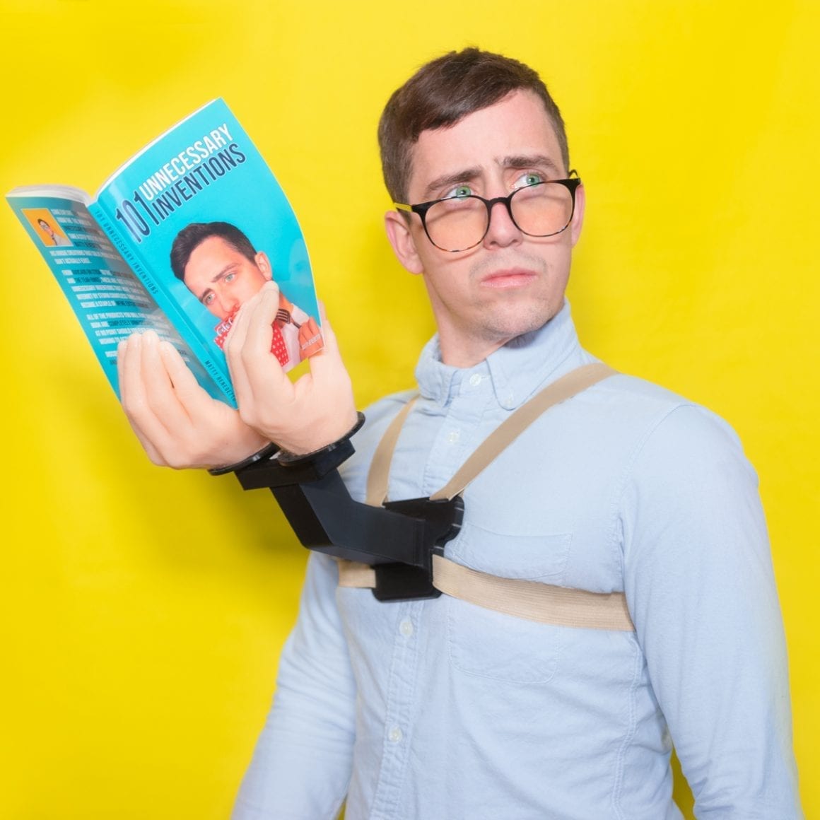 Matty wearing a tan harness with black supports holding an open blue book in front of him.