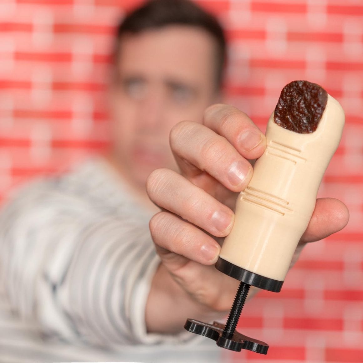 Matty holding a beige artificial finger with a dark beef-jerky nail protruding from the top.