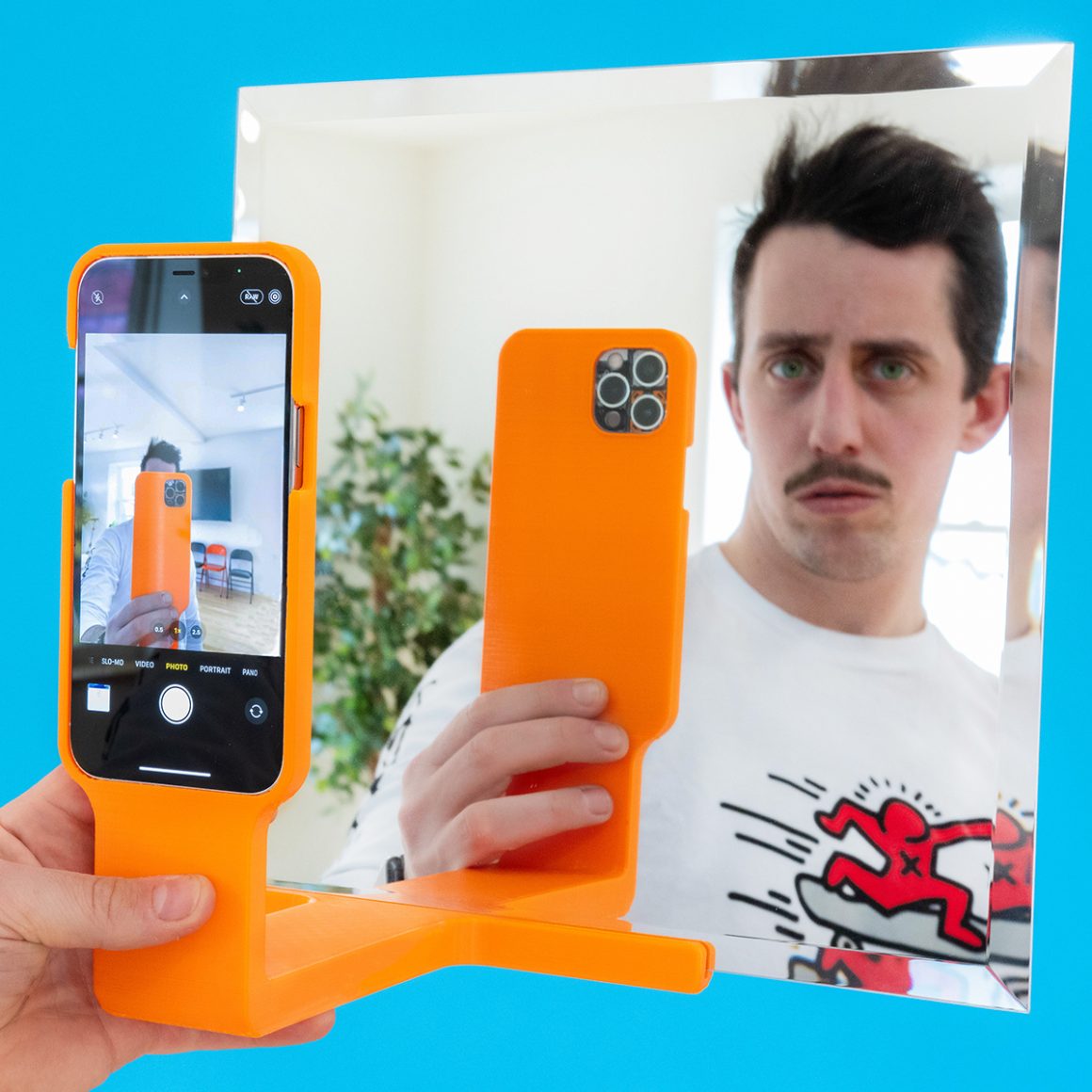 Matty holding an orange phone-and-mirror attachment that reflects his smartphone.